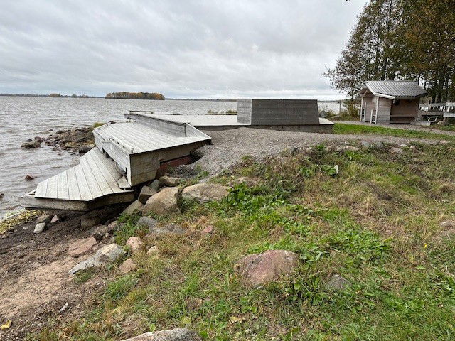 Strand med ett träddäck i olika nivåer. Det finns en liten raststuga i bakgrunden. 