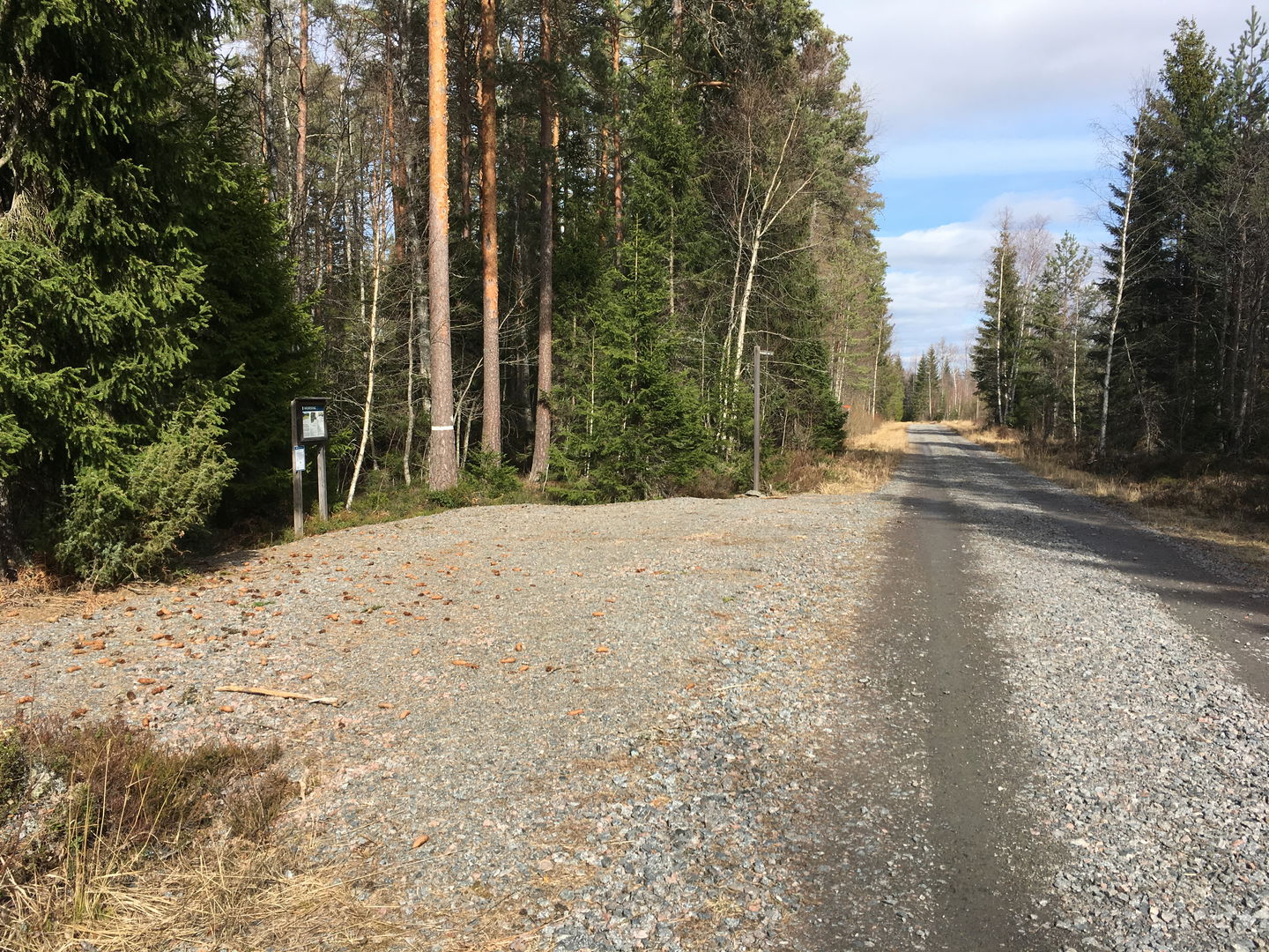 En grusad parkeringsplats vid sidan av en grusad bilväg. På parkeringsplatsen står en informationsskylt.