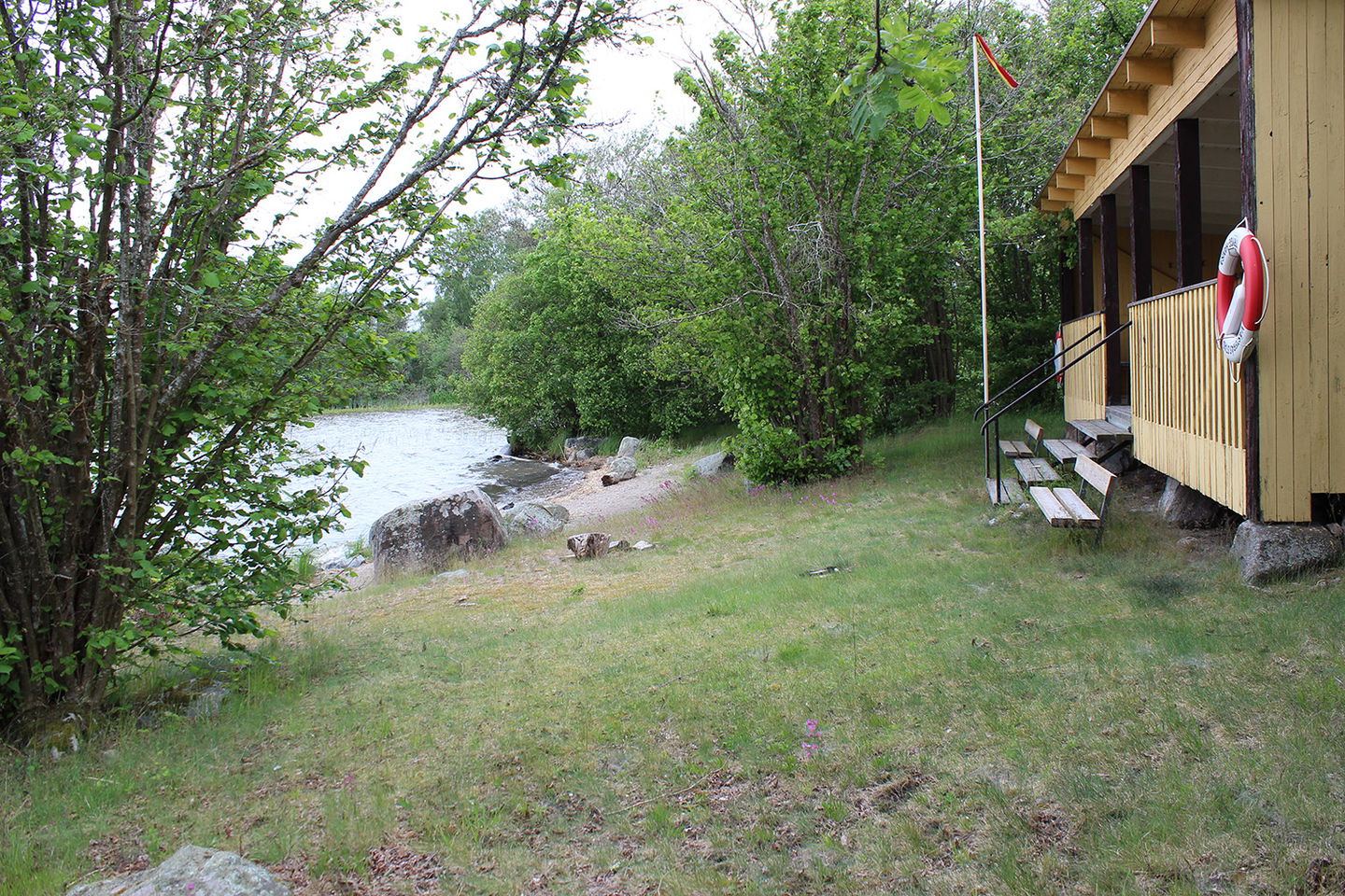 Bild med byggnad för ombyte, sittbänkar och sandstrand.