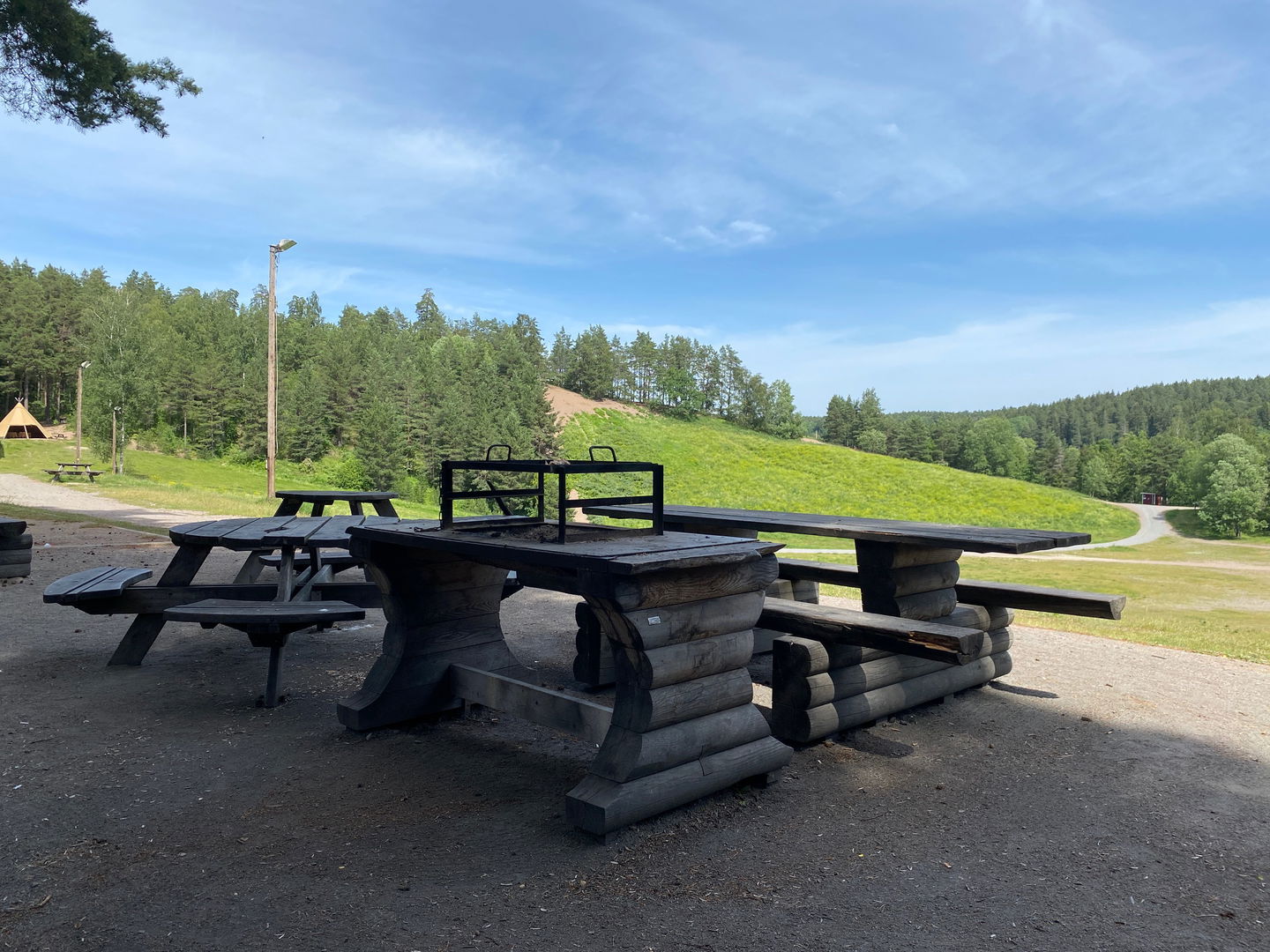 Ett grillbord med grillgaller står på en grusplan uppe på en höjd. Vid grillplatsen finns flera bänkbord. 