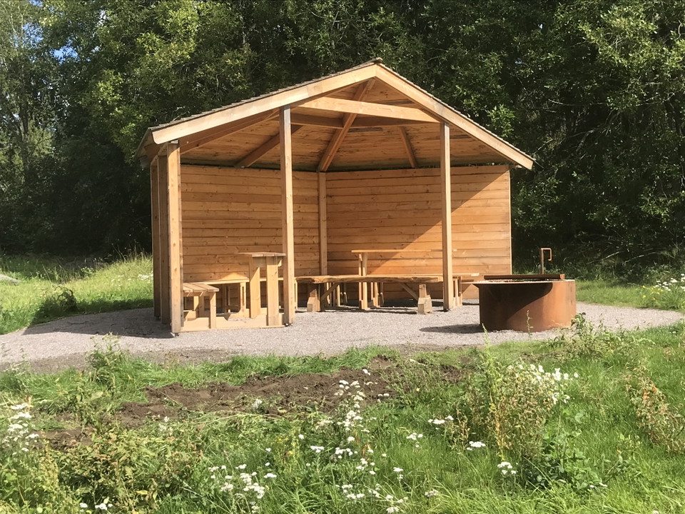 Vindskydd i trä, framför syns en eldstad.