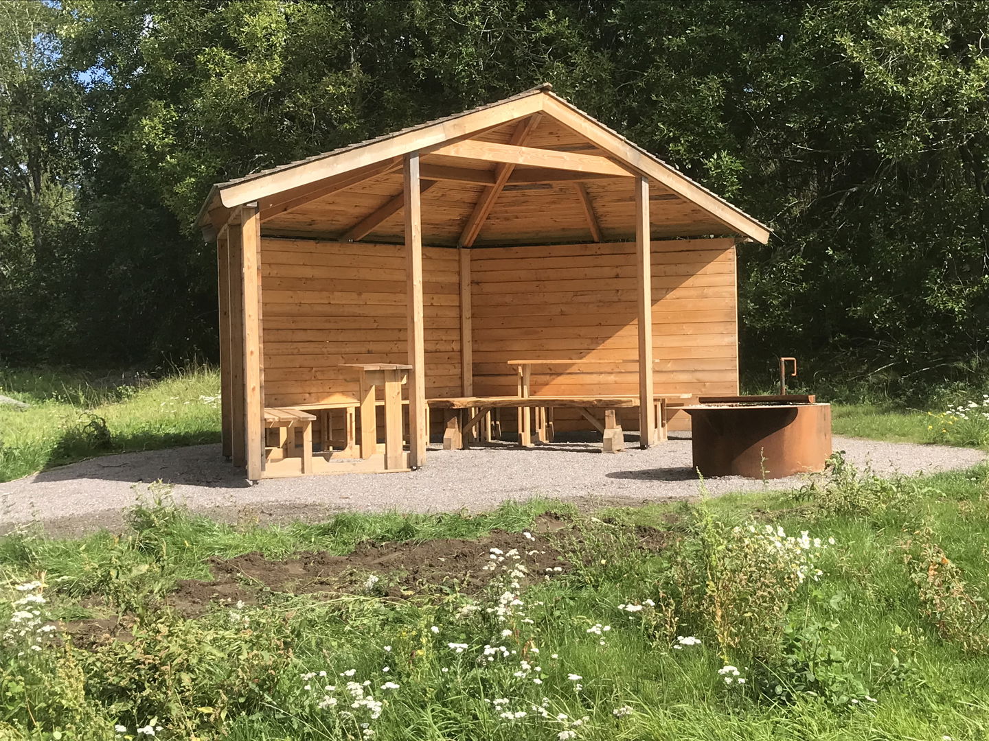 Vindskydd i trä, framför syns en eldstad.