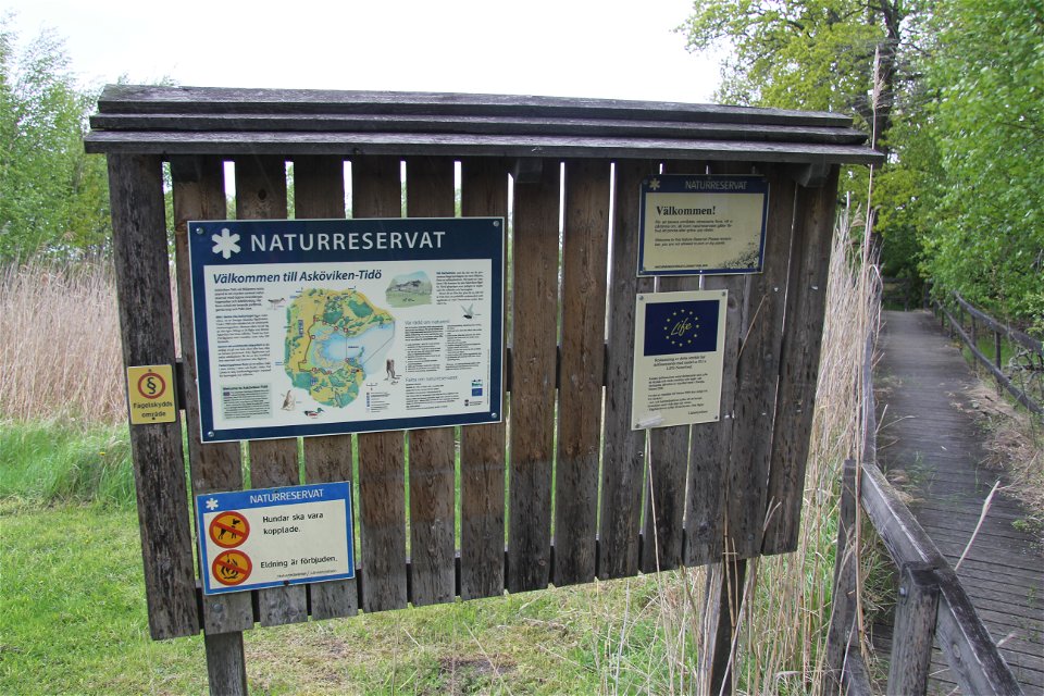 Informationstavla över naturreservatet. Bredvid går en träspång med staket.