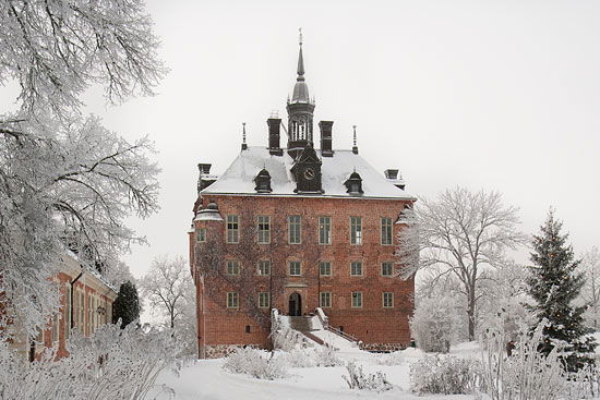 Ett slott med tre våningar och ett torn högst upp. Slottet står i en snötäckt park.