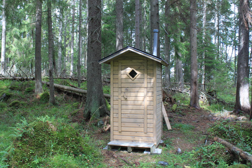 Ett smalt, litet skjul med en skorsten står i skogen.