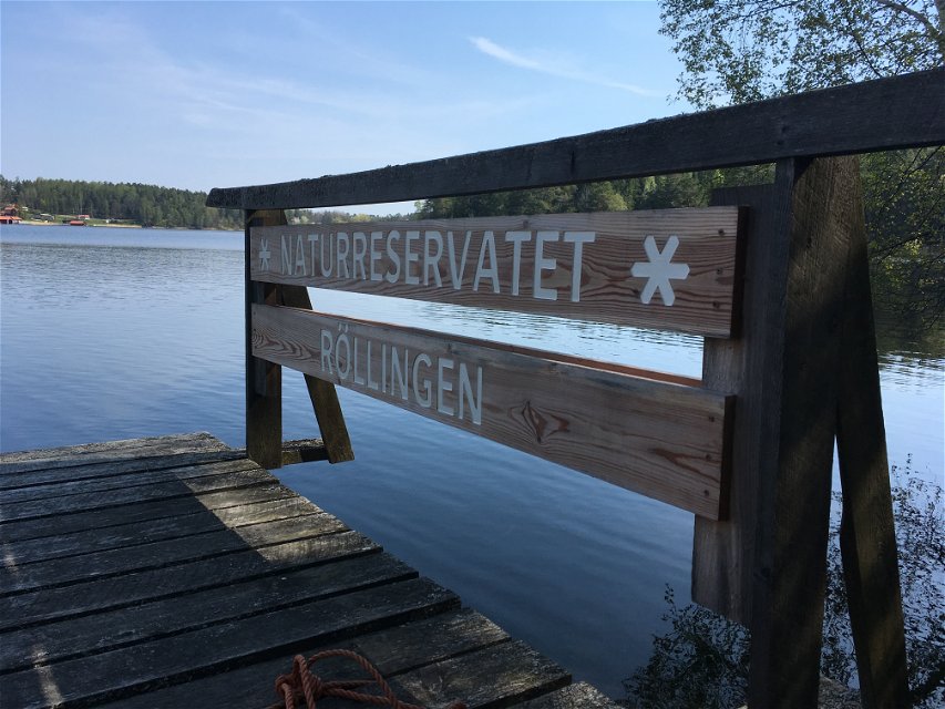 Närbild på en träbrygga vid vattnet. På bryggan finns en skylt med texten "Naturreservalet Röllingen".