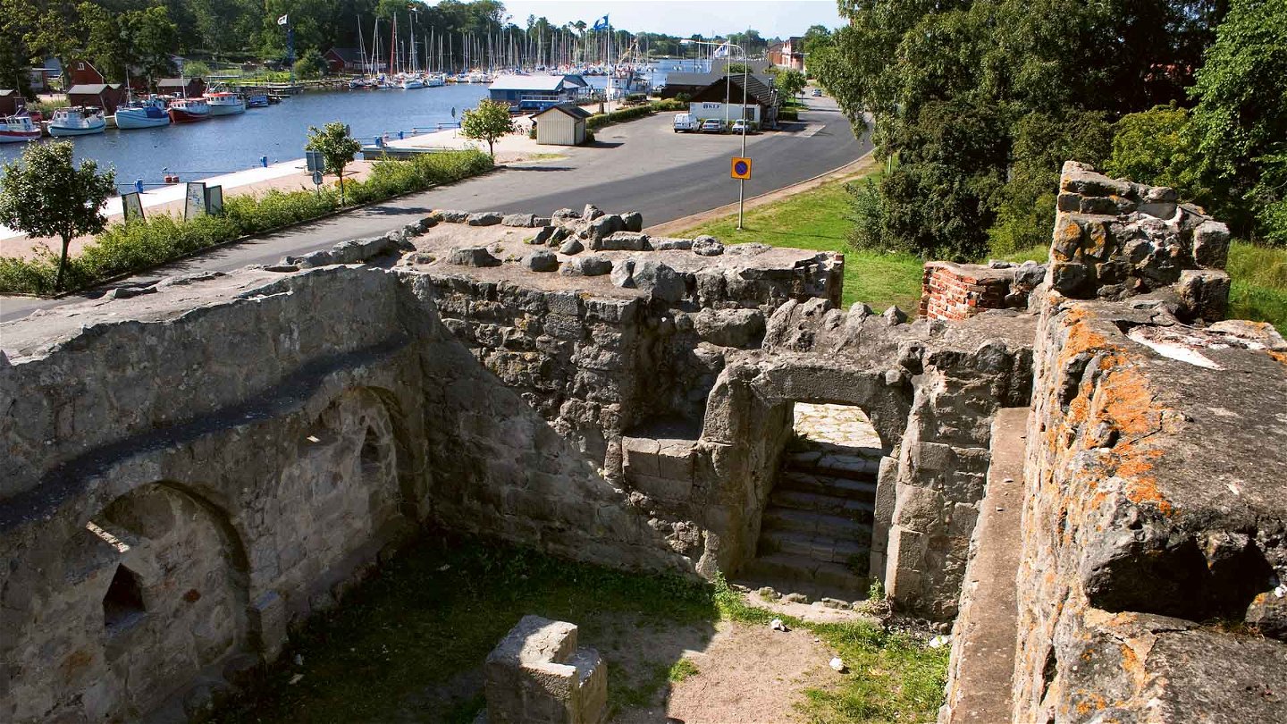 Ruin med ytterväggarna kvar. I bakgrunden skymtar gästhamnen i Åhus.