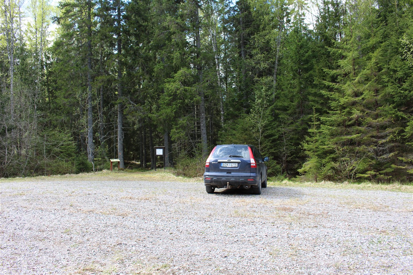 En bil står på en stor grusad parkering med skog framför.