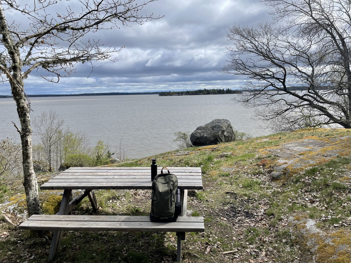 Bord med bänkar på en höjd med utsikt över Mälaren. Vattenflaska och ryggsäck med termos.
