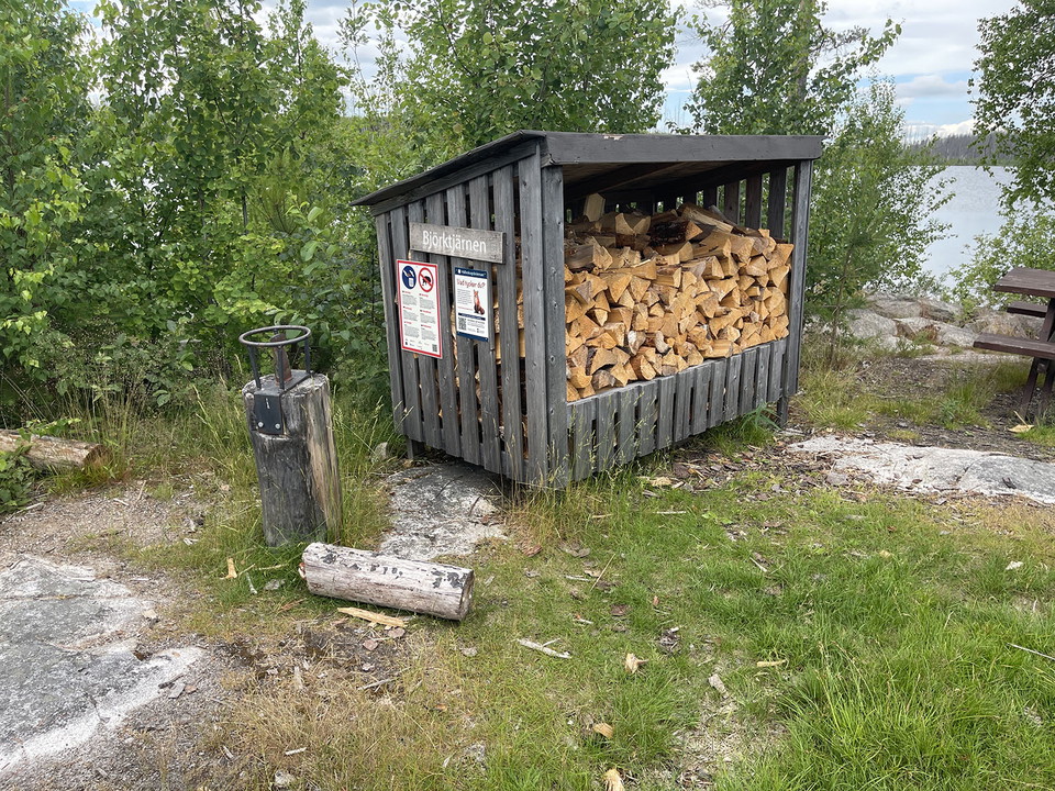 Vedförråd. En fastmonterad yxa finns bredvid.