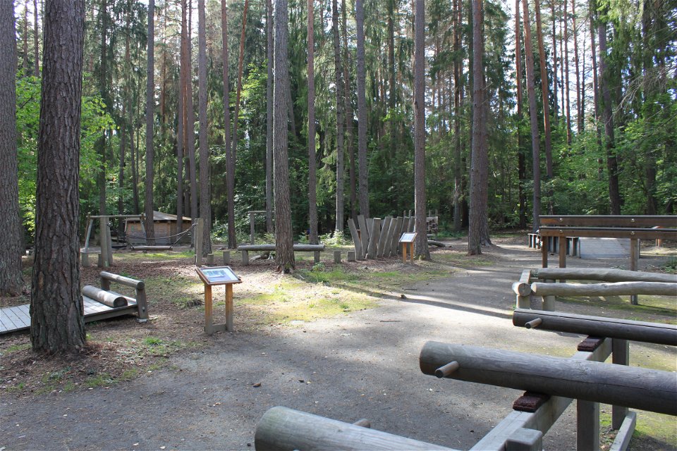 På en plan yta i en skogsglänta står en träningsbana uppställd. Det finns flera olika slags stationer och vid varje station står en informationsskylt.