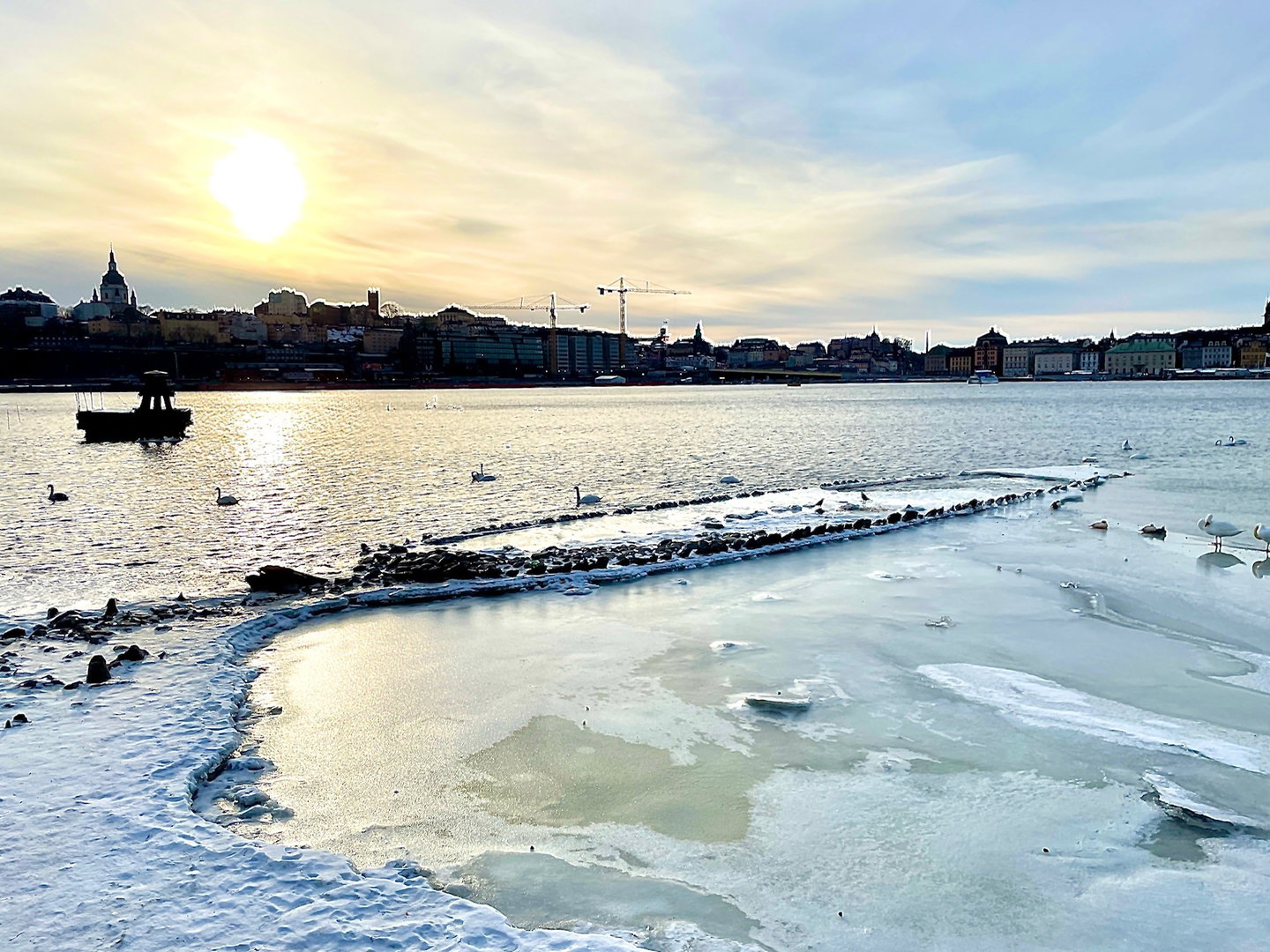 Skeppsvrak sticker upp ur isen med Slussen i motljus i bakgrunden.