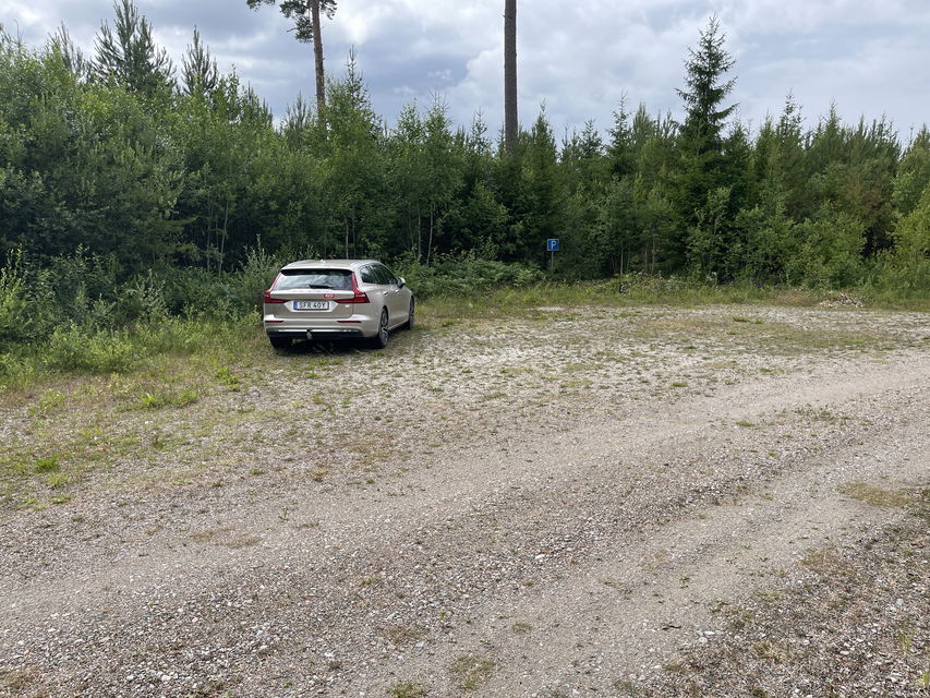 Bil parkerad på en grusad yta. En parkeringsskylt.