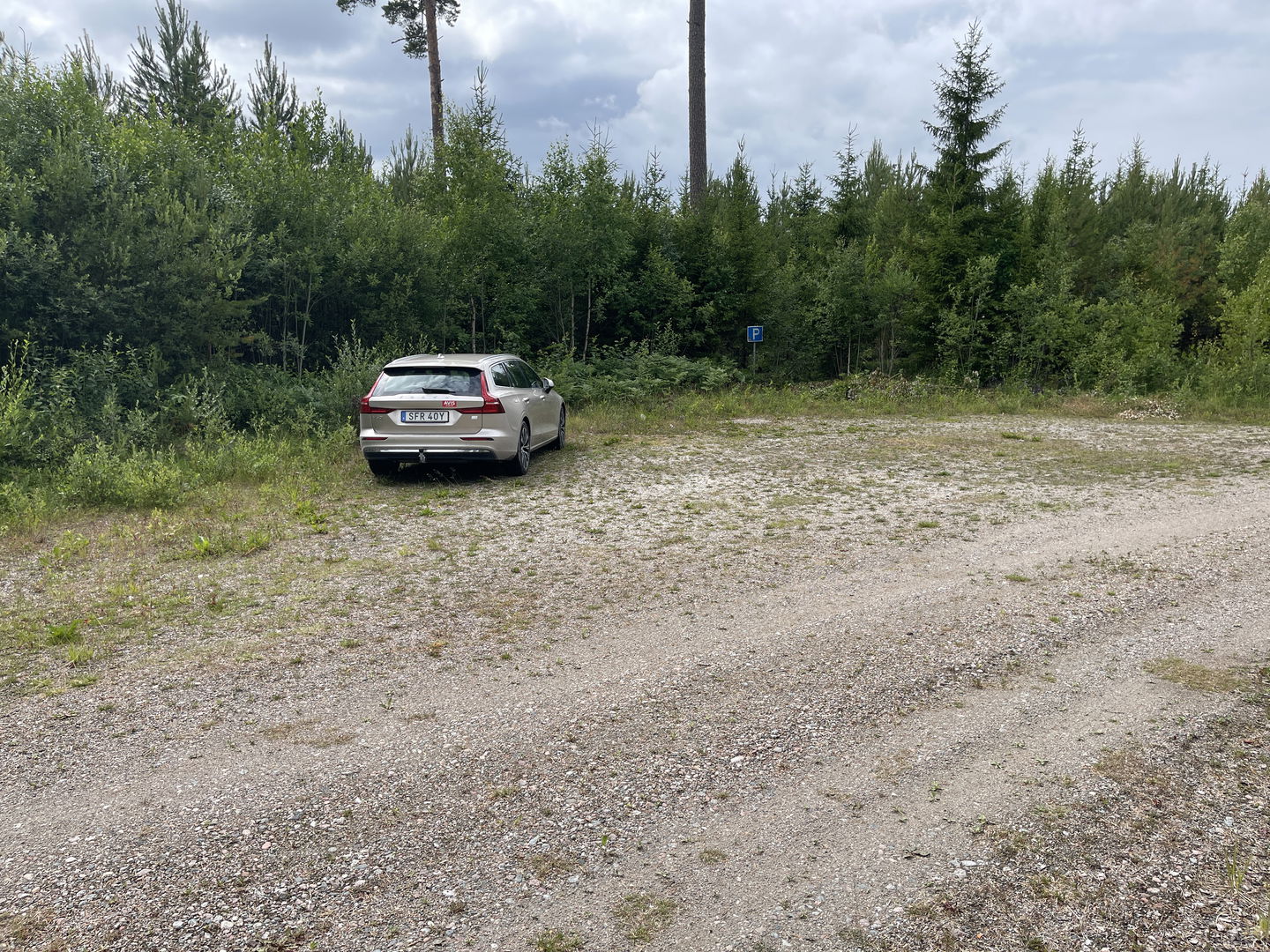 Bil parkerad på en grusad yta. En parkeringsskylt.