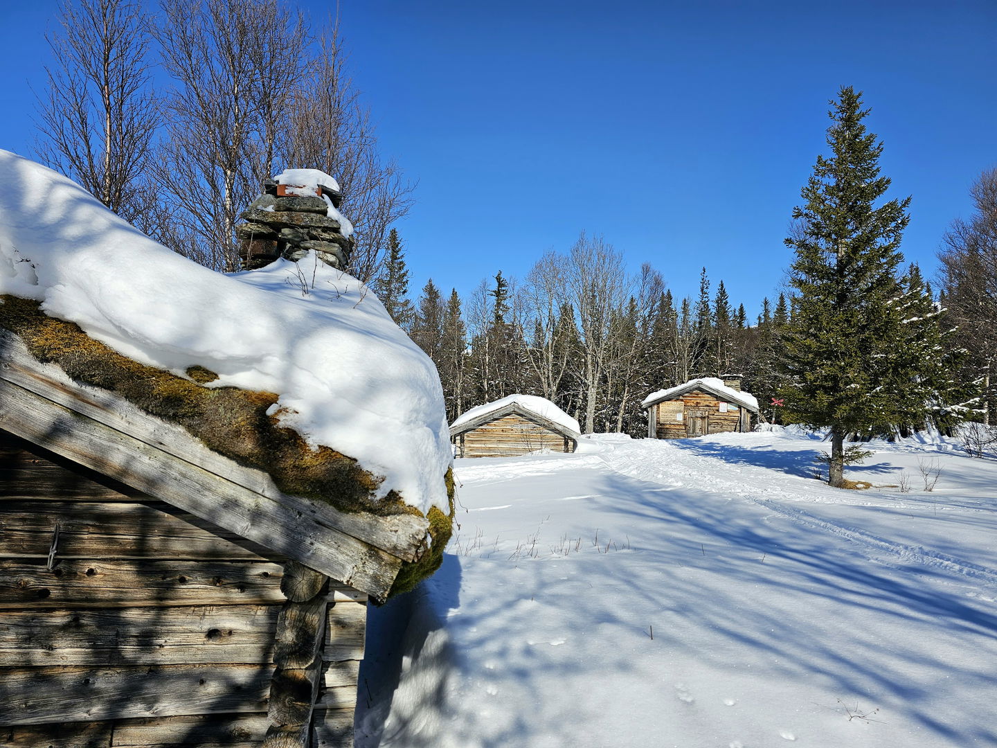 En fäbodvall i vinterskrud med tre hus som syns