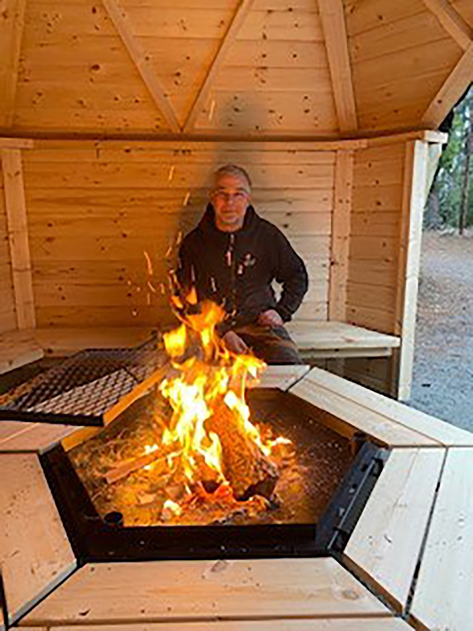 Bild inne från grillkåtan, på en av bänkarna sitter en person och värmer sig vid elden. .