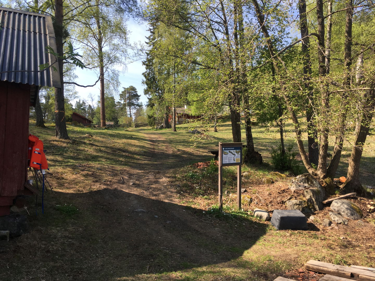 En informationsskylt står nära en bod. Marken lutar svagt uppför och är ojämn.