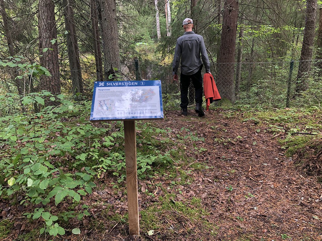 En man står står strax bakom en informationstavla vid ett gruvhål.