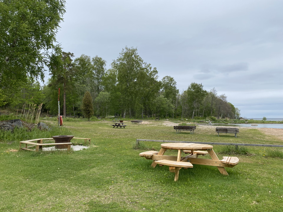 Bänkbord med grillplats i bakgrunden på en gräsmatta vid Ängskärs havsbad