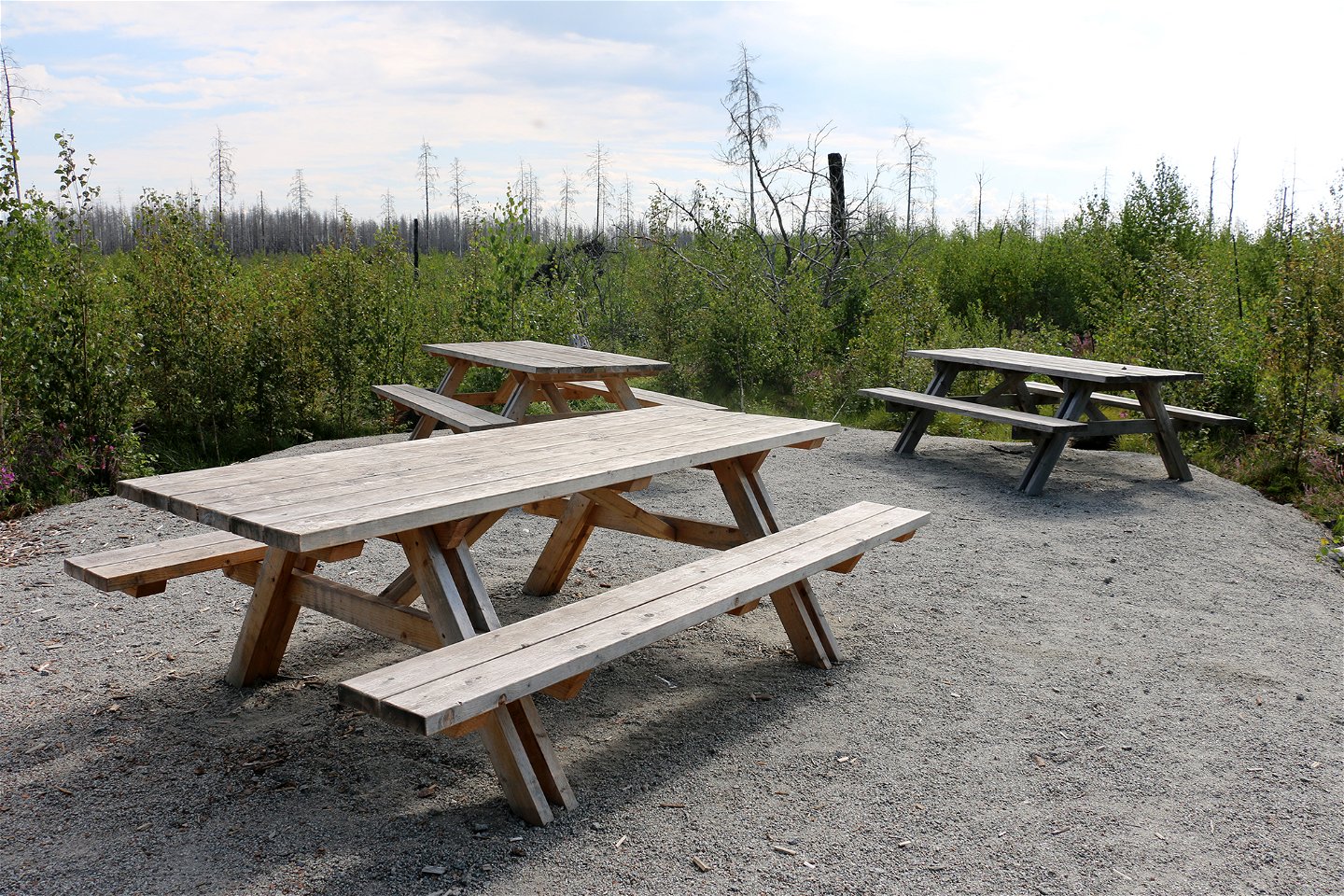 Tre picknickbord i trä på en grusplan.