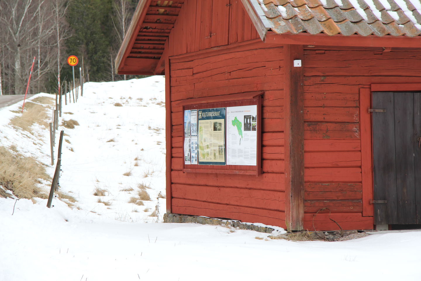 Informationstavla på byggnad intill landsvägen.