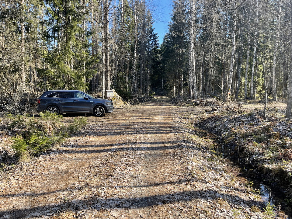En bil står parkerad i en vägficka läns med en skogsbilväg. Bredvid bilen står en informationsskylt.