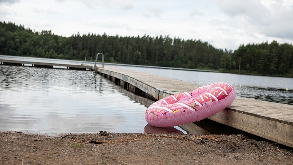En badring som ser ut som en donut vilar mot en brygga vid en sjö
