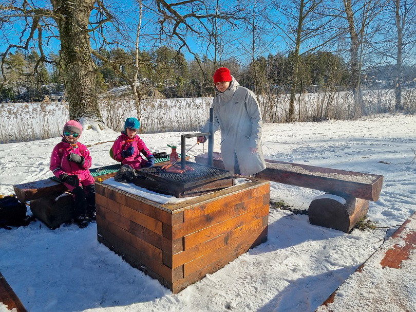 En kvinna och två barn grillar korv