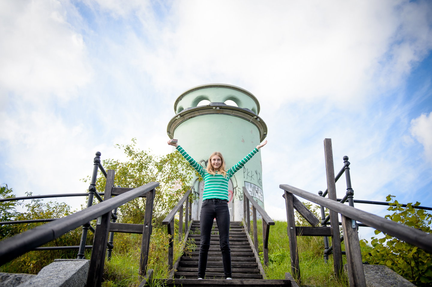 En tjej är glad och hoppar glatt framför det gröna vattentornet