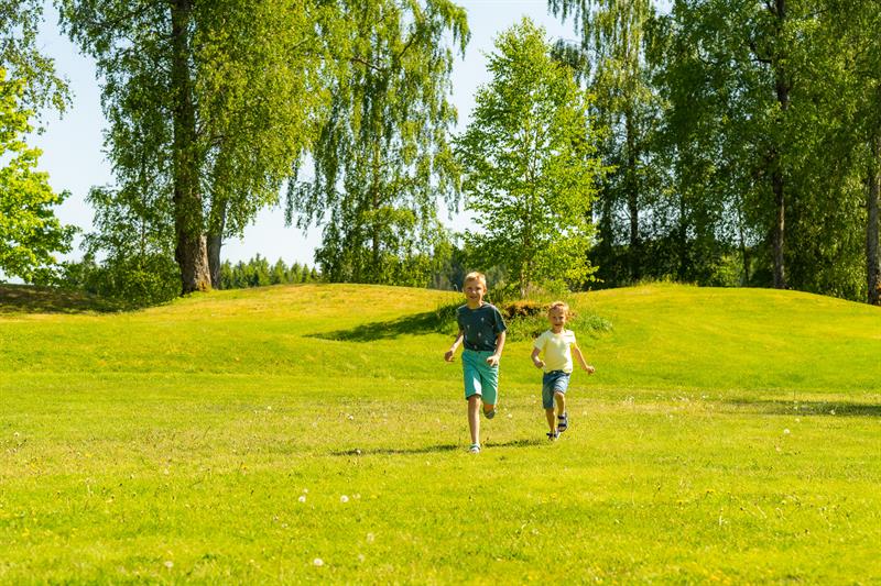 To gutter som løper over gresset med gravfeltene i bakgrunn