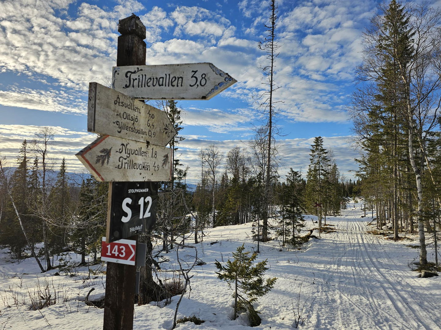 Hänvisningsskyltar på en stolpe bredvid ett skidspår