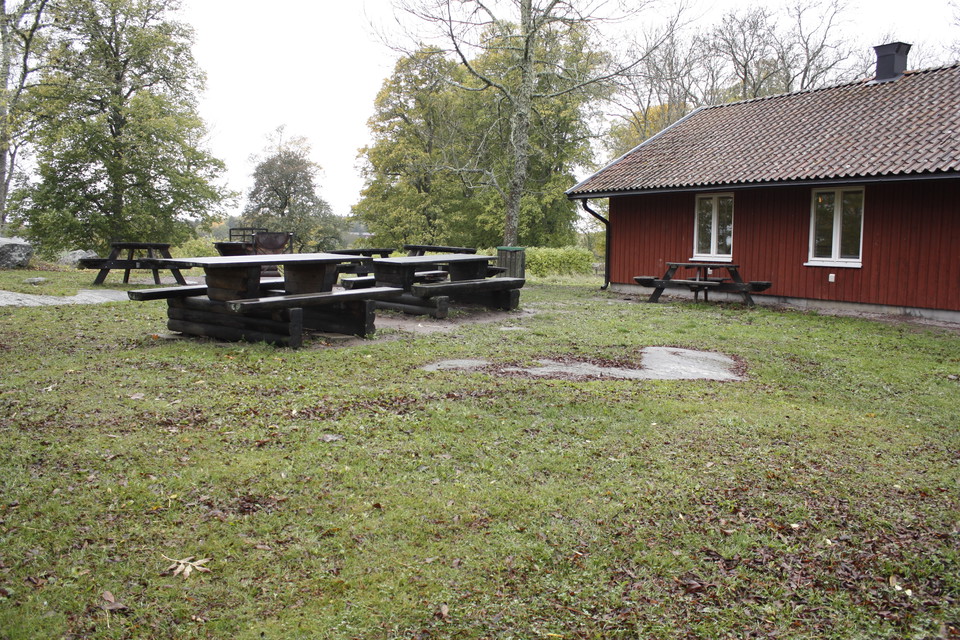 Flera bänkbord står på en gräsyta vid en stuga.