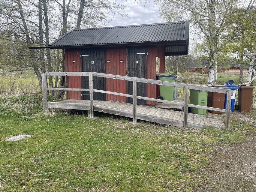 Rödmålat hus med svarta knutar och dörrar. En ramp går upp mot dörrarna.