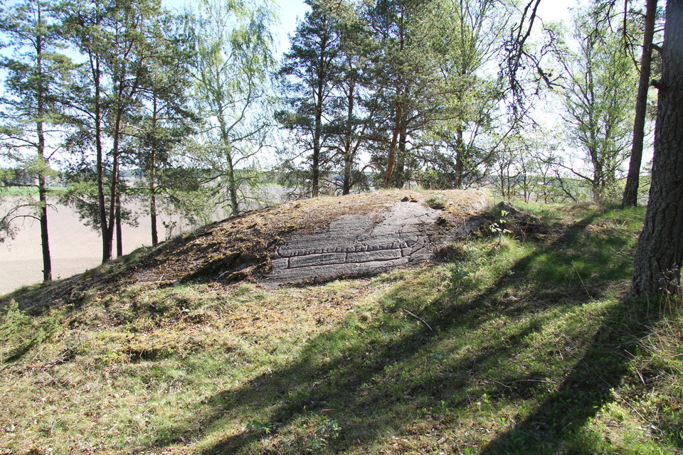 På klipphällen finns ett stort skepp, fotat på håll. Ristningen visar en förenklad bild av hur en riktig båt kunde se ut för 2300 år sedan.