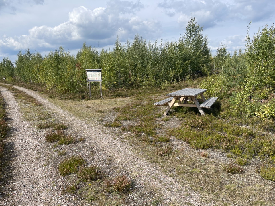 Grusväg som grenar sig. Picknickbord och skylt.