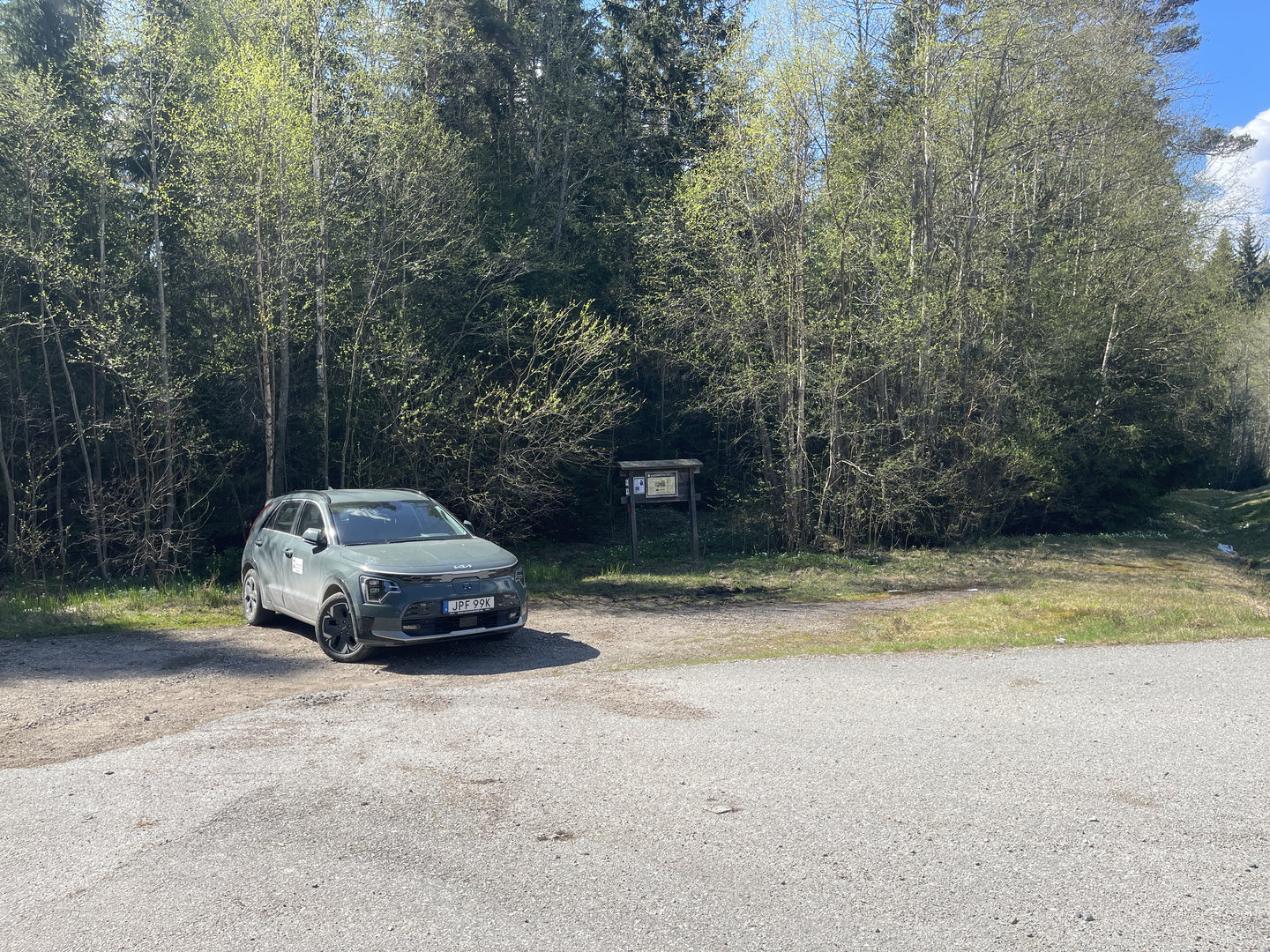 En bil står parkerad vid skogskant.