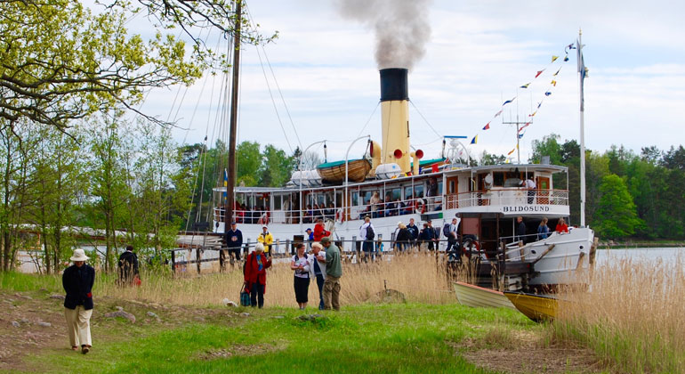Sommar och mulet, en fullpackad skärgårdsbåt lägger till vid Ängsö där människor står och väntar