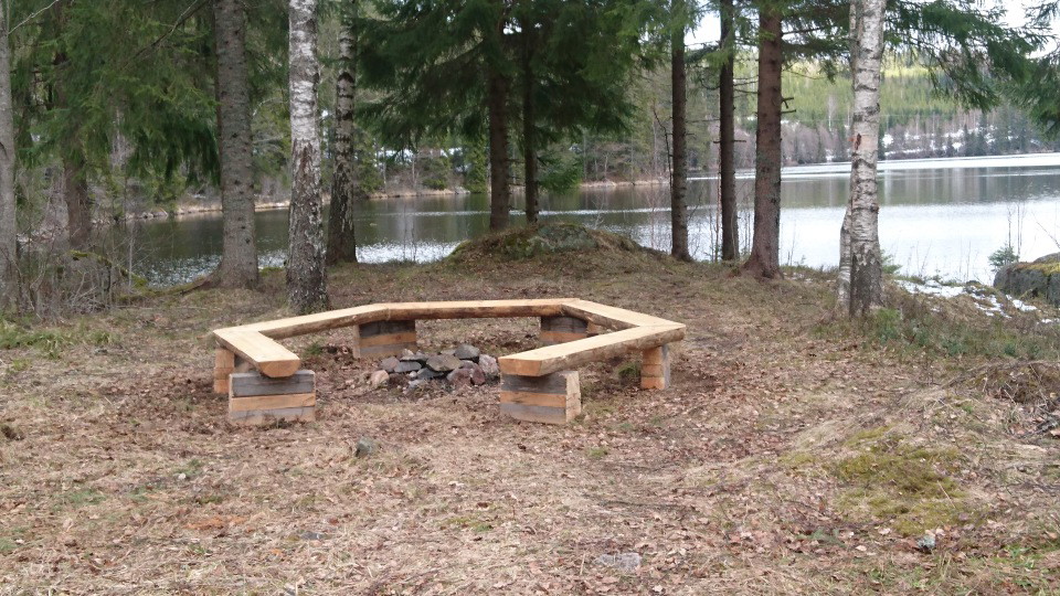 Eldplats med sittbänk runt om vid kanten av sjön.