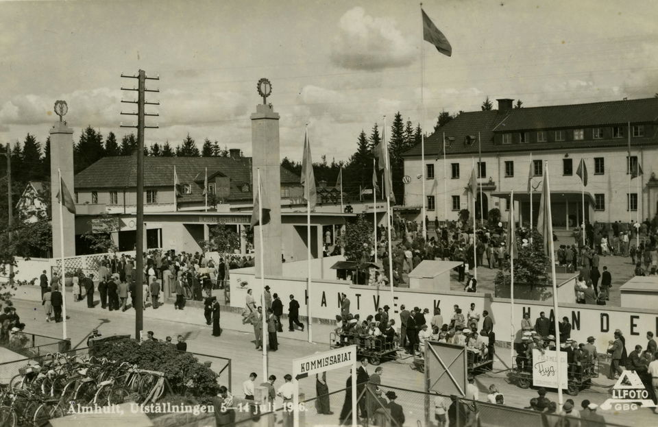 Kö av människor, flaggor och två rejäla pelare vid entrén. I bakgrunden syns Gemöskolan.