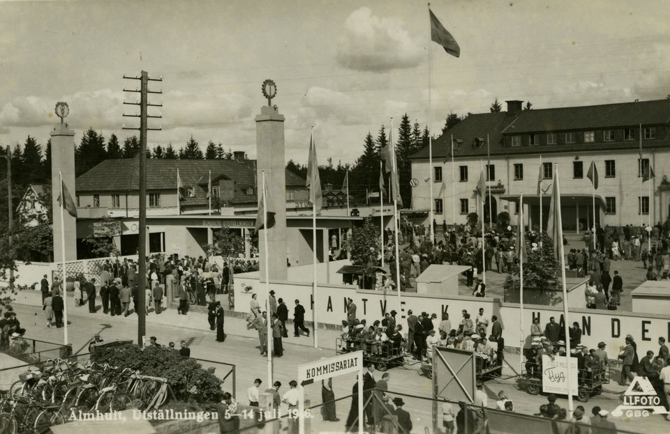 Kö av människor, flaggor och två rejäla pelare vid entrén. I bakgrunden syns Gemöskolan.
