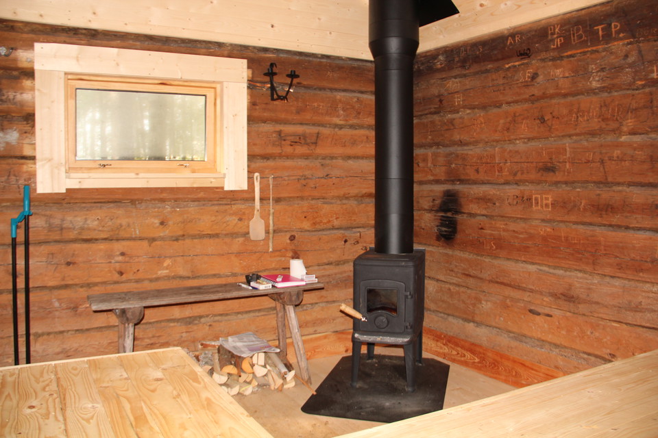 Inne i stugan: liten kamin hörnet och väggar i stockvirke.