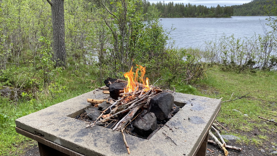En eldstad vid en sjö med skog runt omkring.
