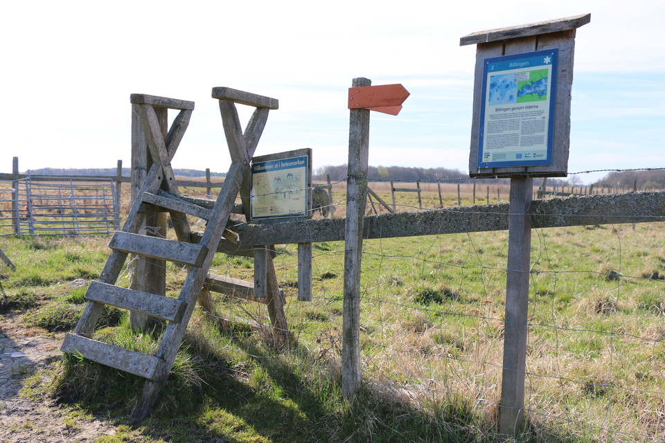 Stätta, en enklare trapp som går över ett staket. Orangepilar som visar vägen. Informationsskyltar och hagar.