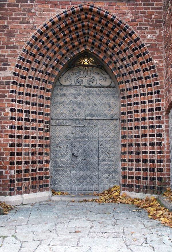 Portal in till kyrkan, i rött tegel med sirliga entrédörrar