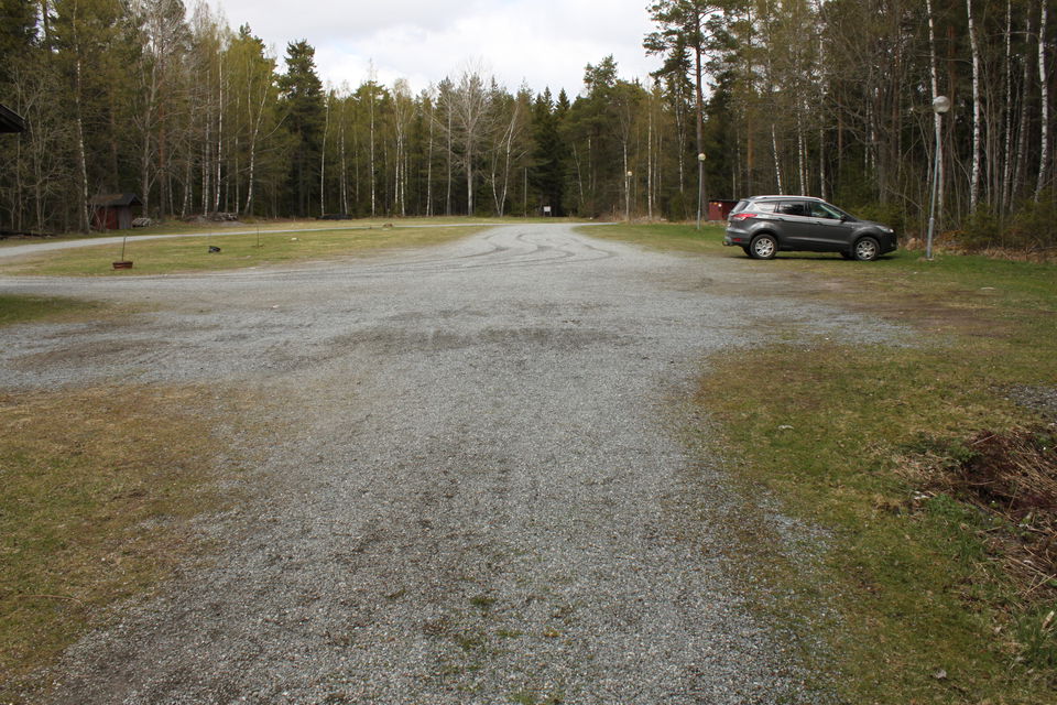 En bil står på en mycket stor grusad parkeringsplats med gatubelysning.