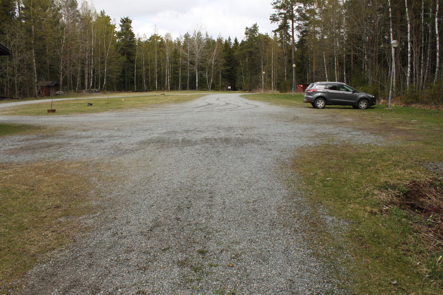 En bil står på en mycket stor grusad parkeringsplats med gatubelysning.