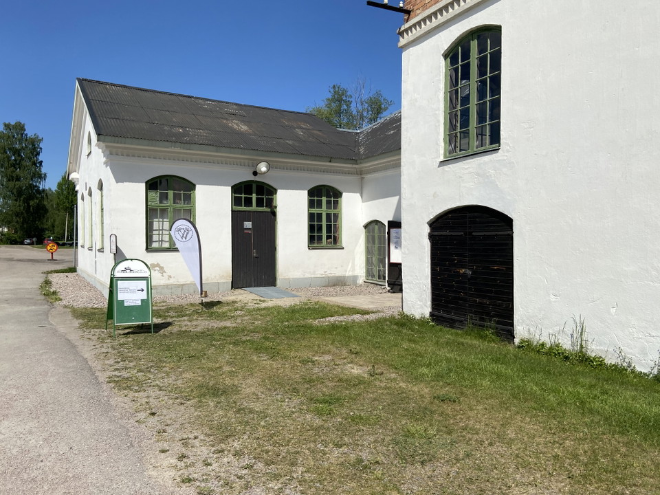 Äldre vit stenbyggnad med trädörr som är ingång till Strömsbergs besökscentrum. 
