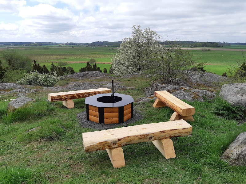 En grillplats med tre sittbänkar står uppe på en höjd. Marken är något ojämn med gräs och stenhällar. 