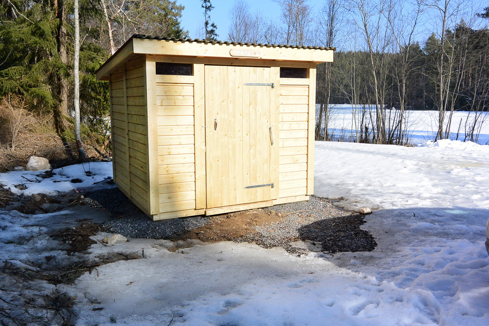 Liten byggnad i trä med dörr och två smala ljusöppningar vid taket.