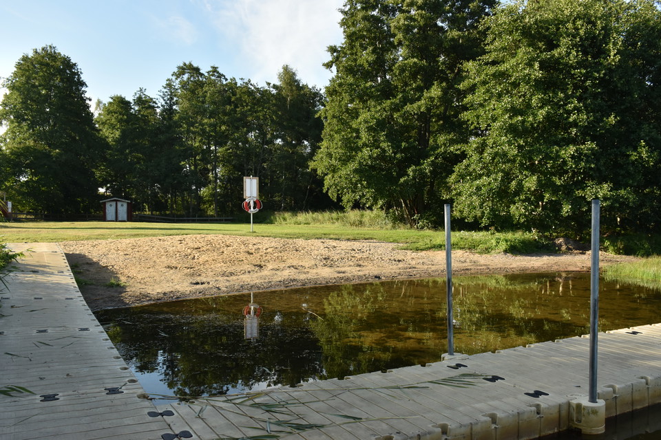 Gräsmatta och sandstrand sett från från brygga.